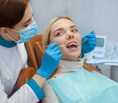 Professional dentist wearing medical mask, examining teeth of a female patient, copy space. Orthodontist working with her client. Beautiful woman having dental checkup. Professionalism concept